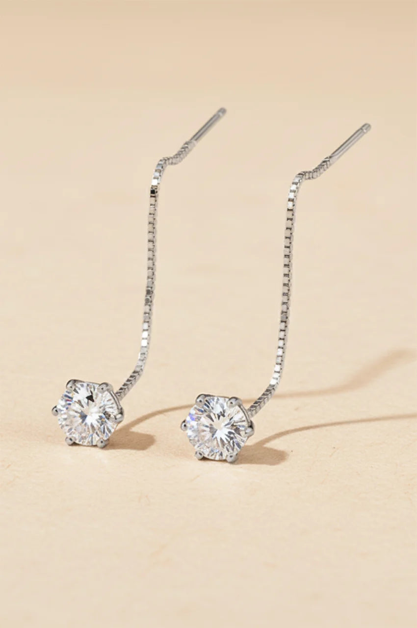 Minimalist silver pull-through threader earrings with solitaire moissanite gem on beige background.