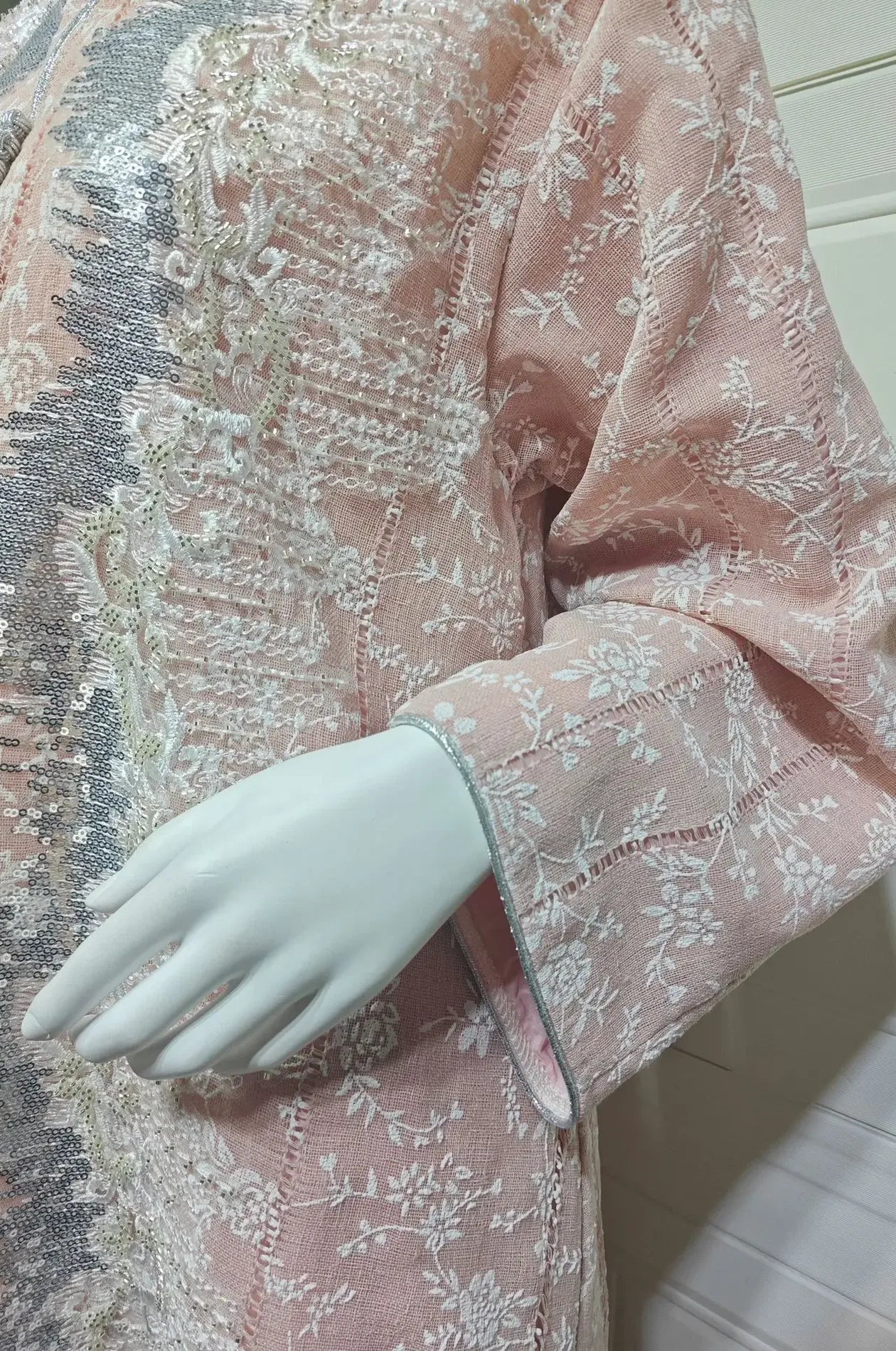 Extreme close-up of the blush pink kaftan fabric showcasing the intricate white floral embroidery and silver sequin textures.