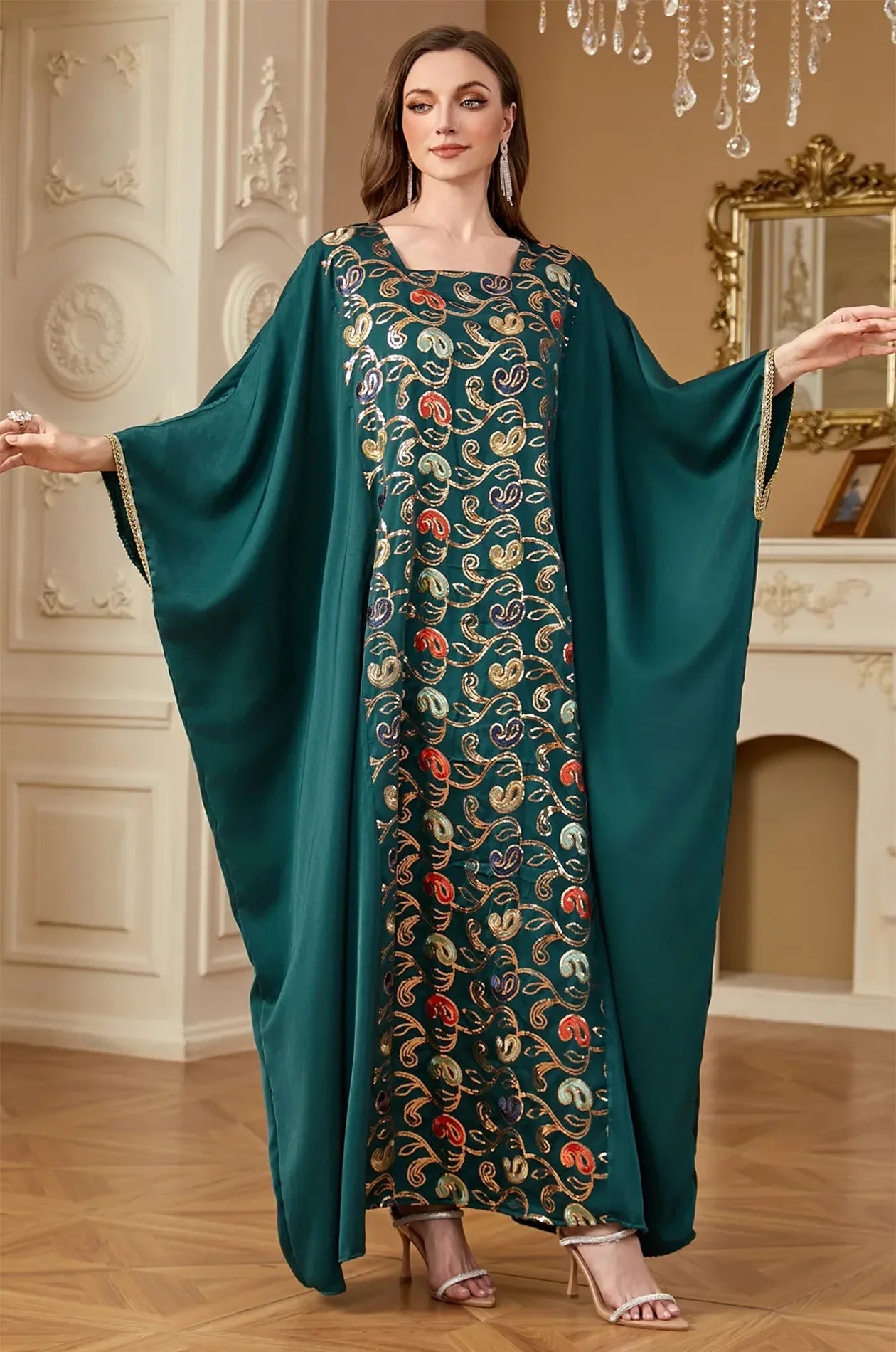 Model showcasing the wide butterfly "Farasha" wings of the green Amiri kaftan with gold braided edges.