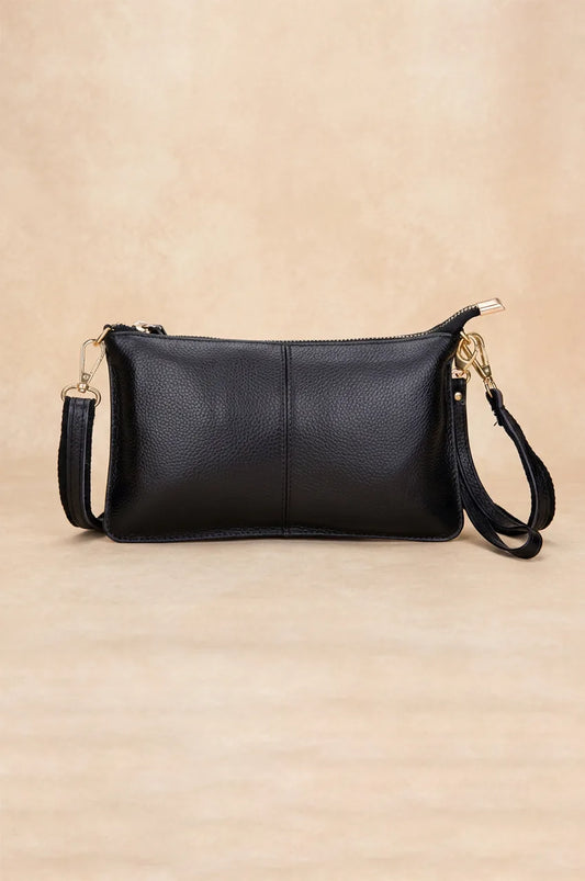 Front view of the black genuine leather crossbody clutch with gold hardware on a beige background.