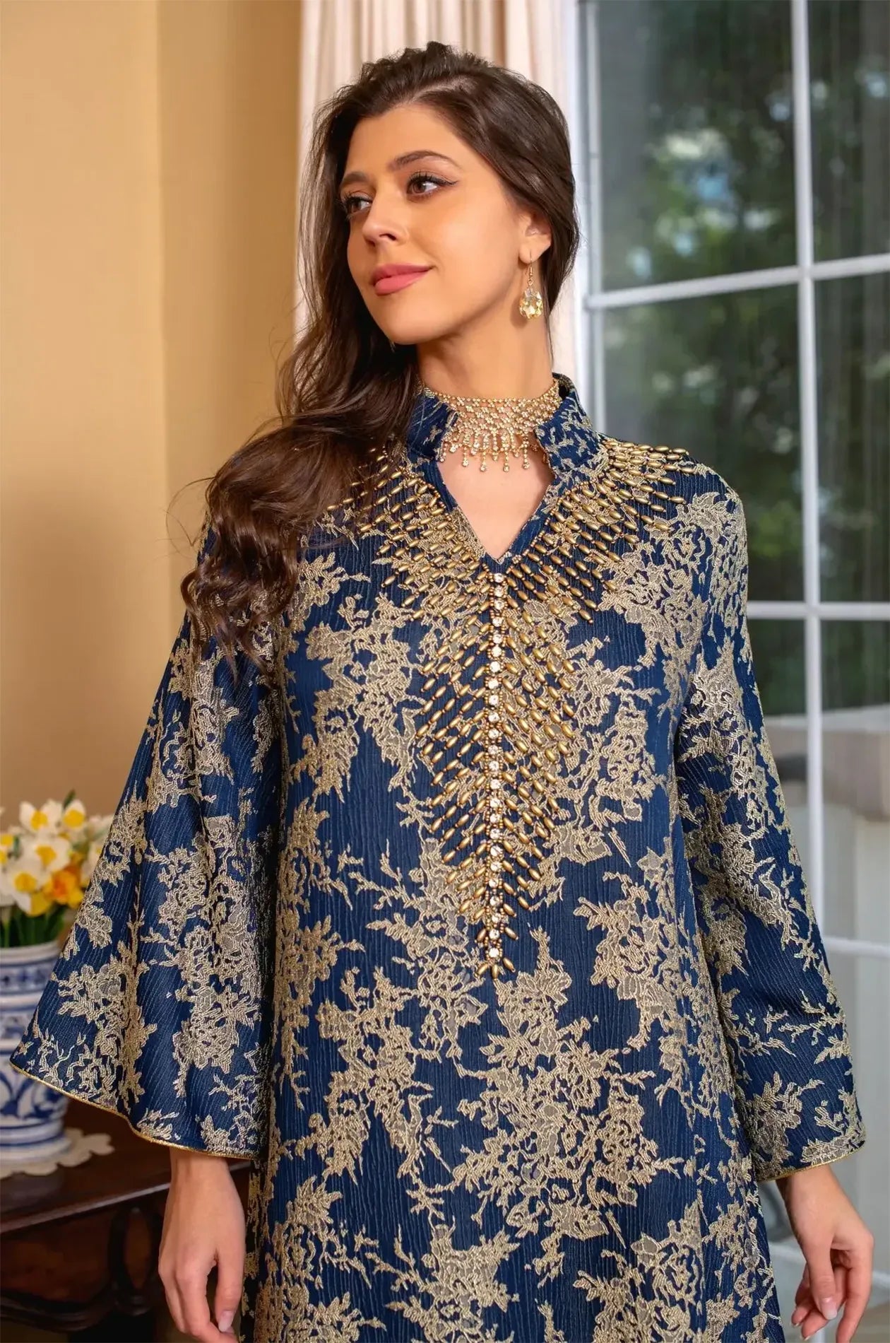 Close-up portrait shot focusing on the intricate gold cascading beadwork and V-neckline of the navy blue Estel kaftan.