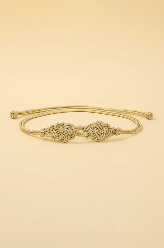 Front view of simple gold braided rope belt with knot details on beige background.