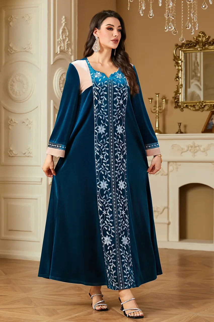 Front view of Lylah teal blue velvet kaftan with silver embroidery standing in luxury room.