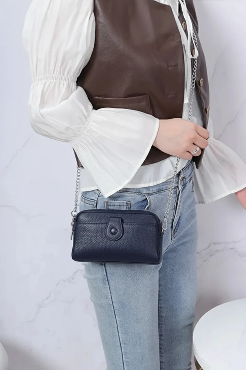 Woman modeling the navy blue leather dual-zip crossbody bag with silver chain strap.