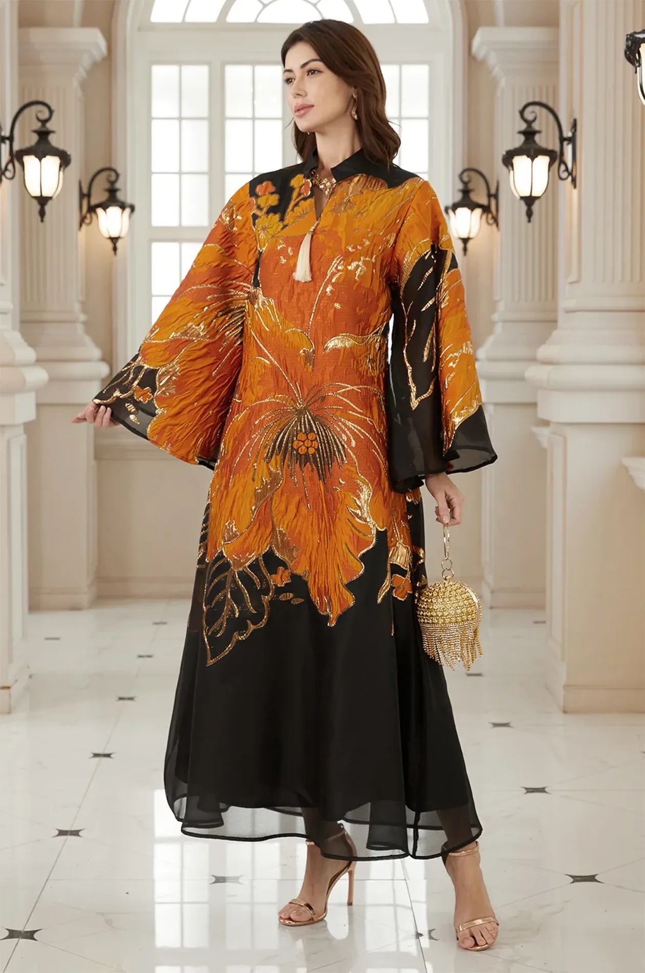 Posed model wearing the Naeli Orange Flowy Kaftan with a gold metallic clutch in a luxury architectural setting.