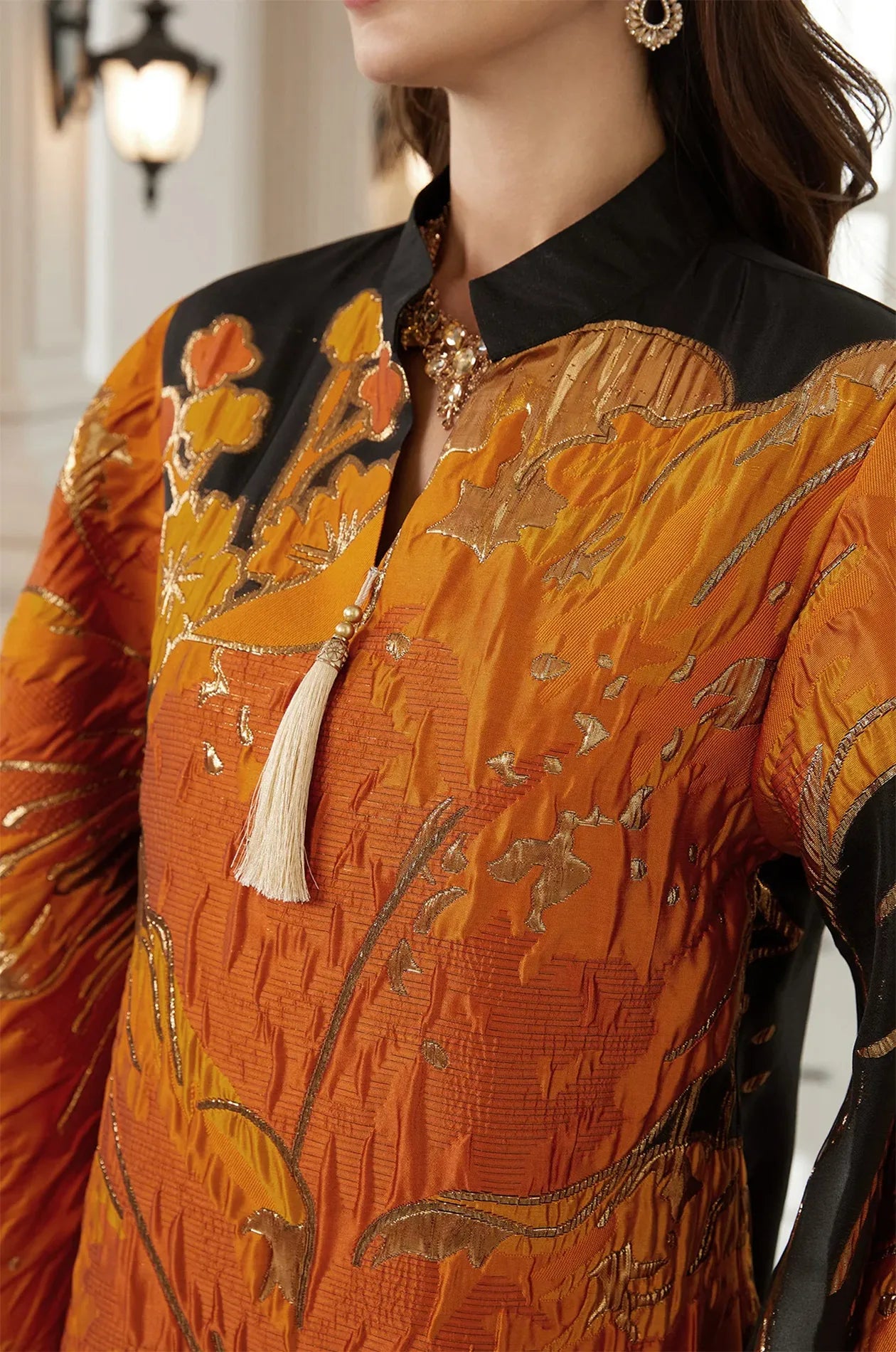 Detailed close-up of the Naeli Orange Kaftan's V-neckline, silk tassel, and shimmering metallic floral embroidery.