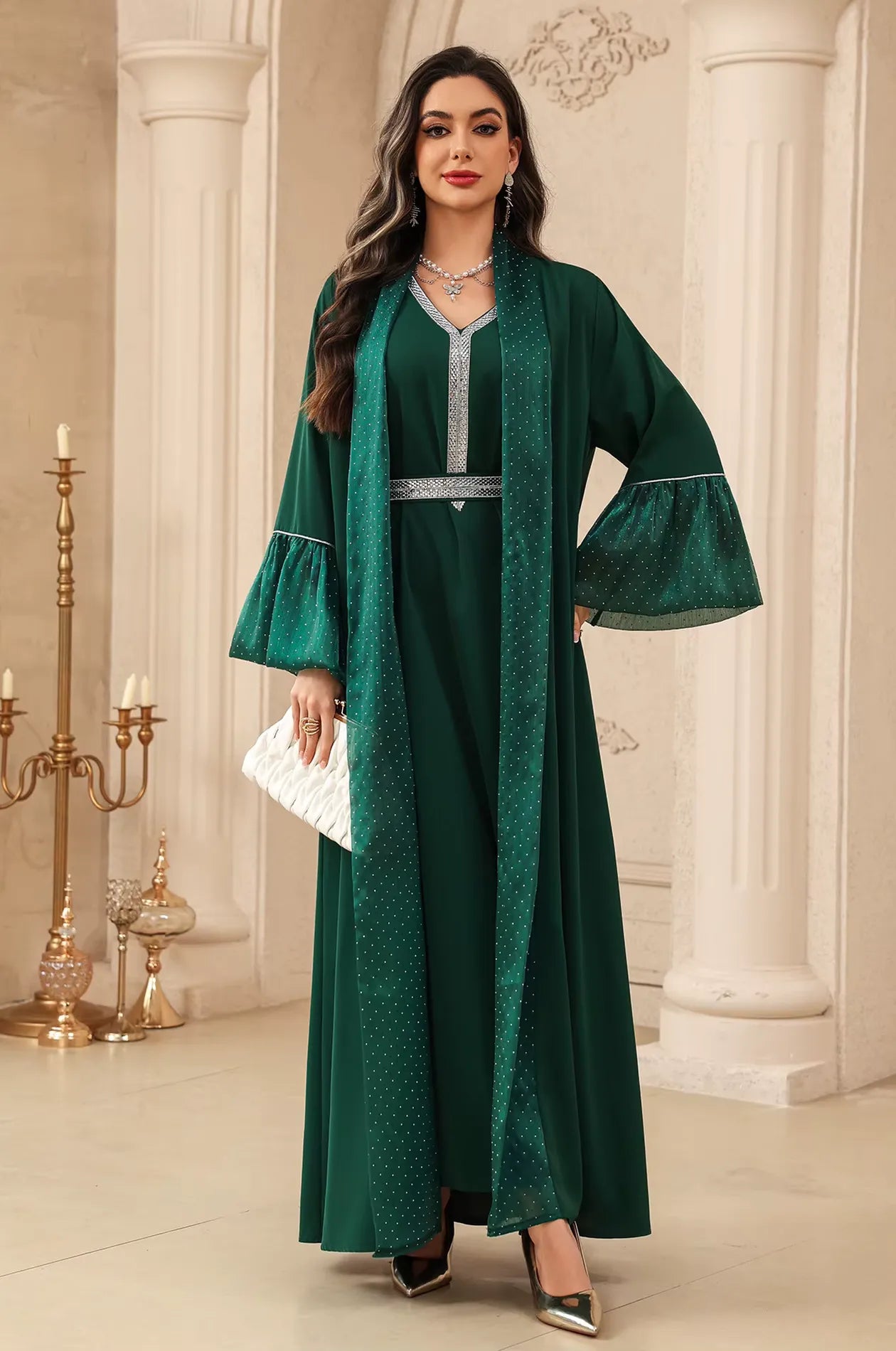 Elegant emerald green Auris Kaftan with silver rhinestone trim, styled with a white textured clutch for a formal event.