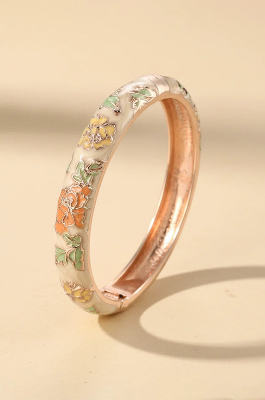 Cream colored enamel bracelet with orange and yellow flowers standing upright.