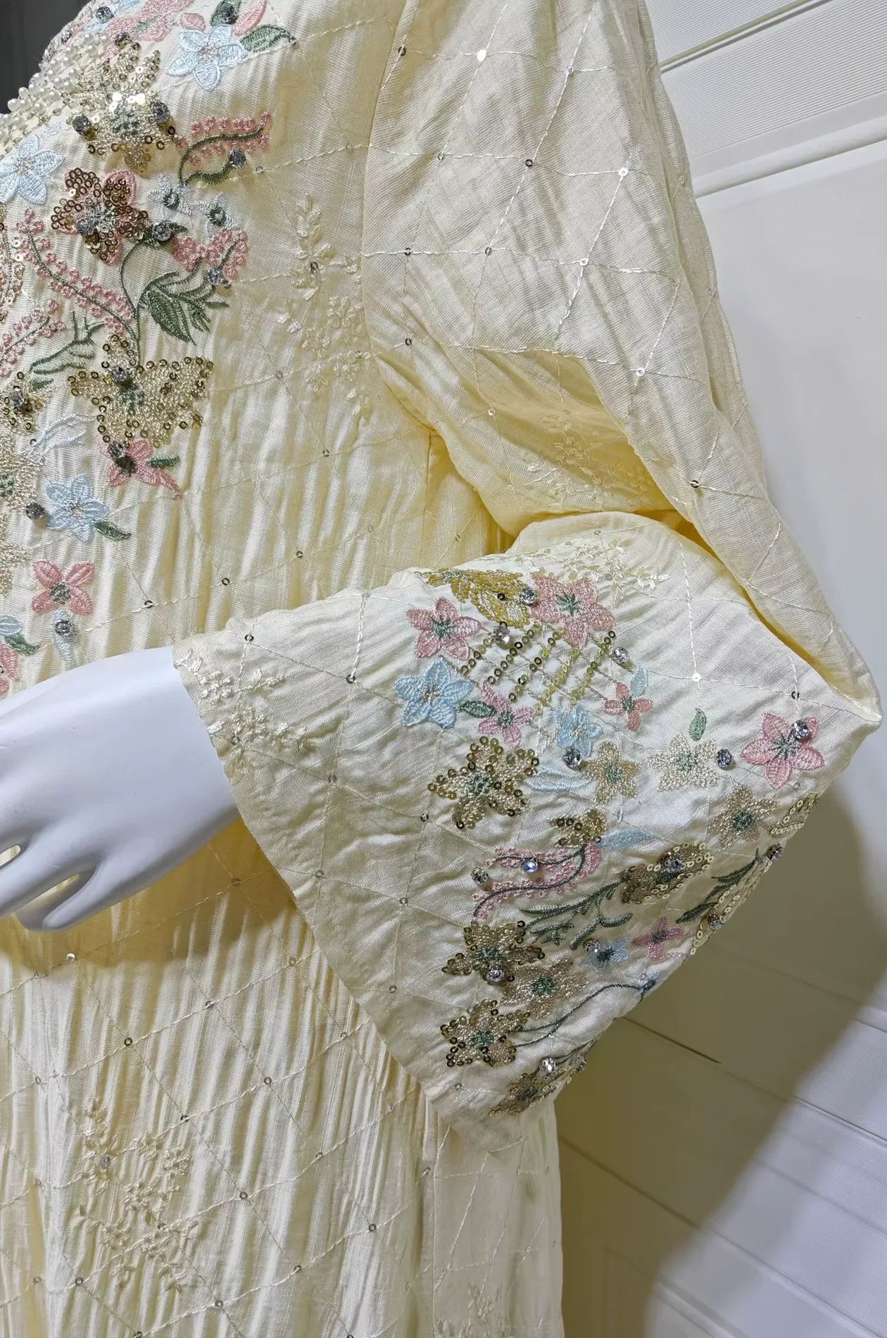 Extreme close-up of the pastel floral embroidery and beading on the sleeve of the beige Equis modest kaftan.