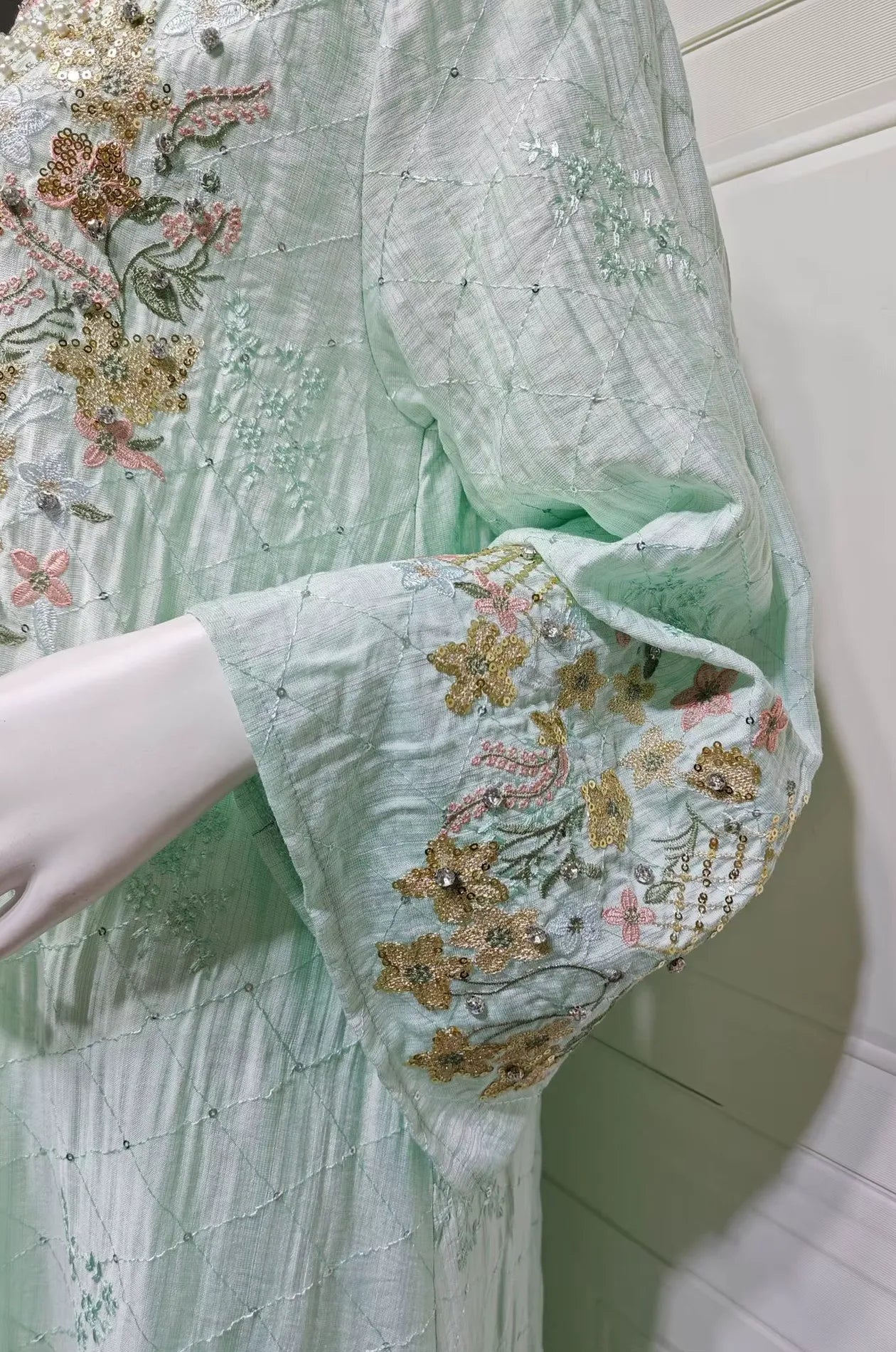 Close-up of the intricate floral embroidery and rhinestone embellishments on the sleeve of the green Equis modest kaftan.