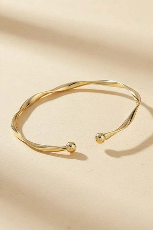 Minimalist gold twisted open cuff bracelet on beige background.