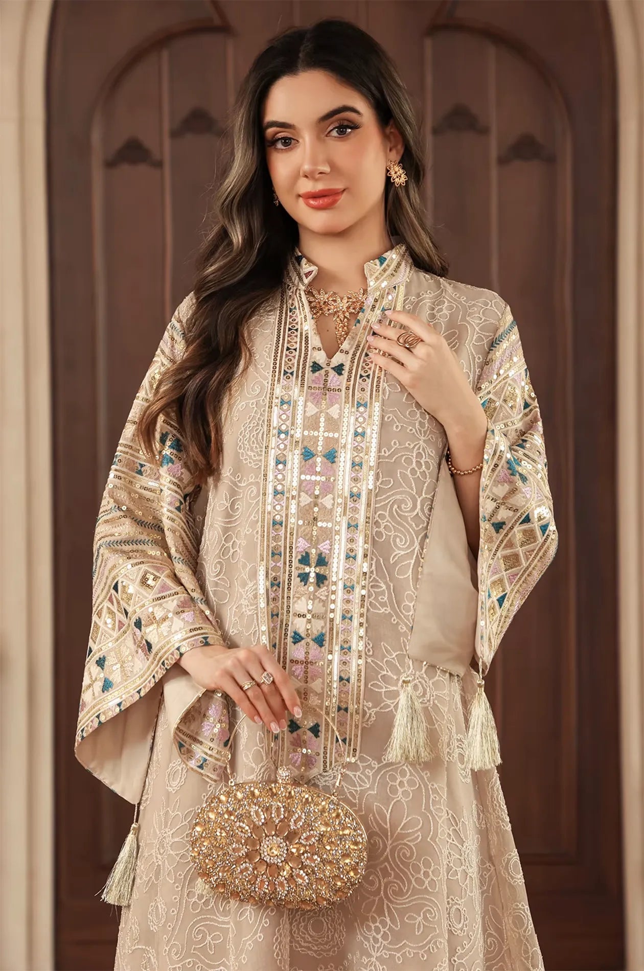 Half-body view of the apricot beige Orla kaftan styled with a gold clutch and V-neck sequin detailing.