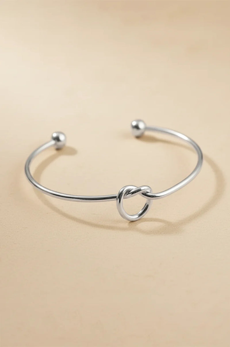 Polished silver tone bangle bracelet with ball ends and central knot.