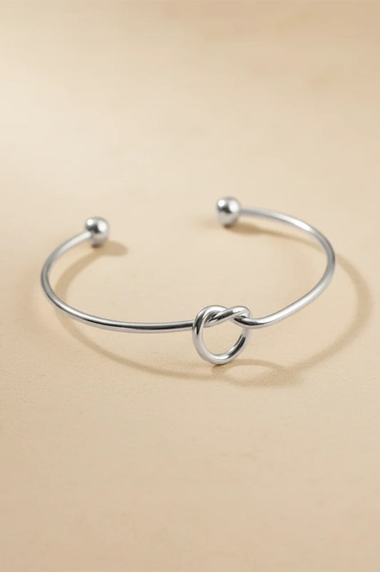 Polished silver tone bangle bracelet with ball ends and central knot.