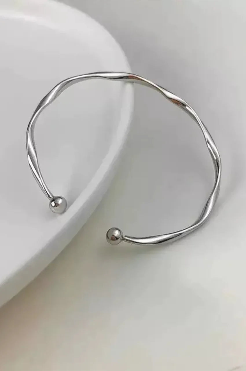 Top down view of silver twisted cuff bracelet on white display dish.