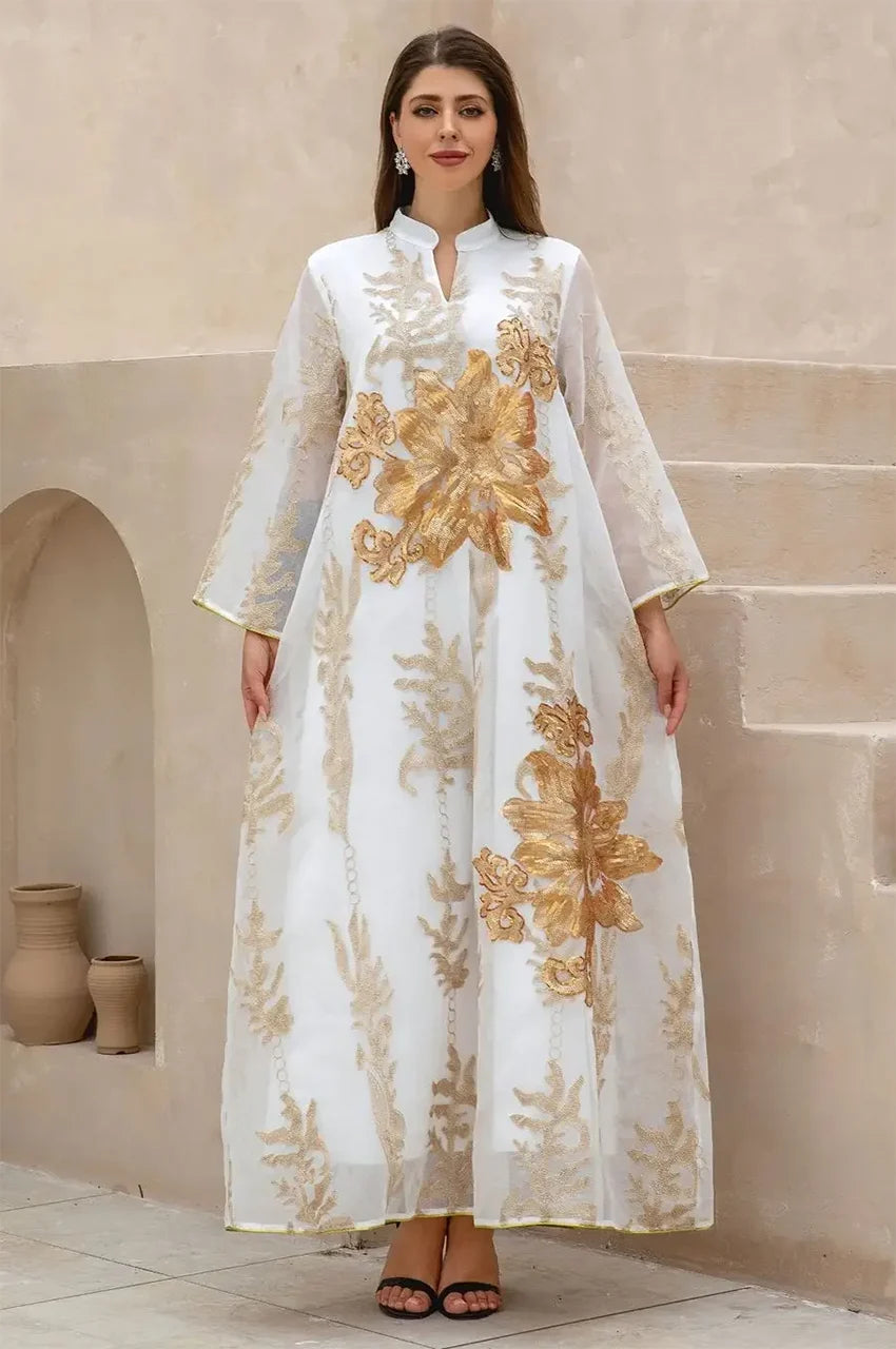 Full-length shot of the white Maliya flower kaftan with gold embroidery against a minimalist desert architectural background.