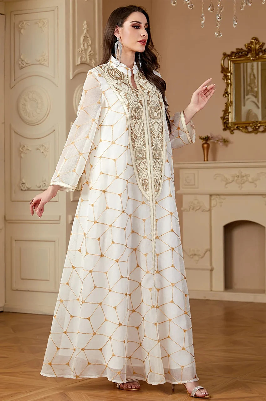 Woman walking wearing Rahel long white kaftan with gold geometric patterns and central embroidery.