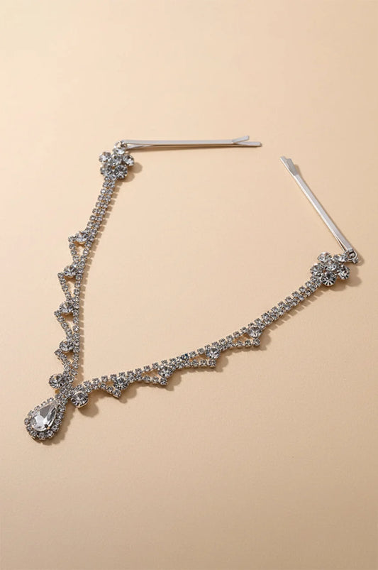 Full view of silver rhinestone forehead headpiece with teardrop crystal and hair pins on a beige background.