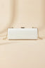 Front view of white patent leather cylinder evening bag with gold clasp and chain attachment points.