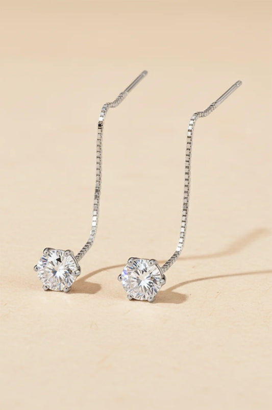 Minimalist silver pull-through threader earrings with solitaire moissanite gem on beige background.
