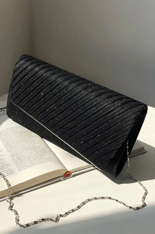 Side angle of black evening bag on white surface showing diagonal pleated structure and silver chain strap.
