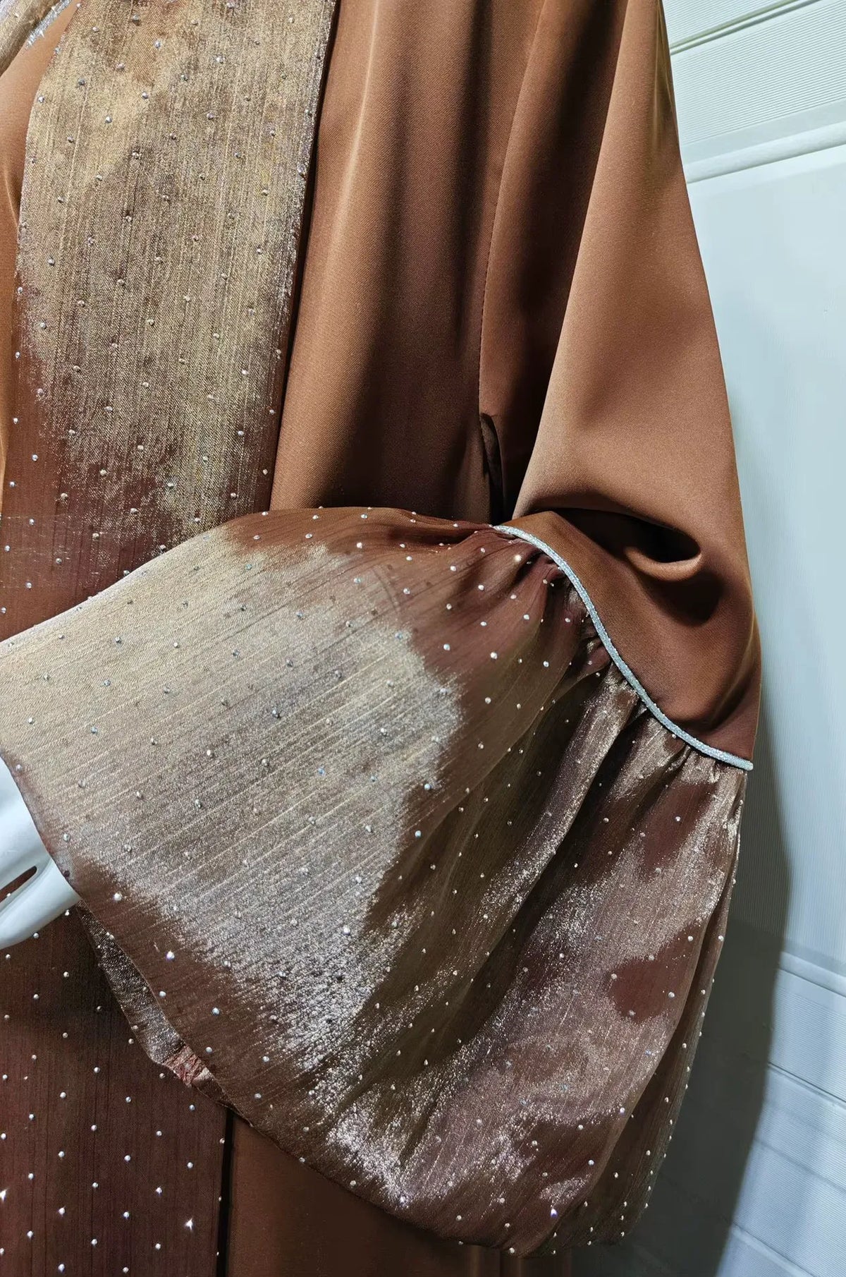 Macro shot of the Auris Brown Kaftan fabric, highlighting the glitter-dot texture and the silver piping on the sleeves.