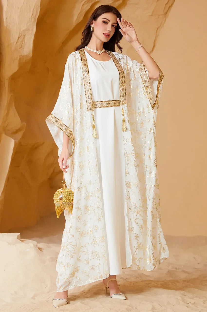 Detailed view of the shimmering gold floral foil and leaf patterns on the white long open kaftan fabric.