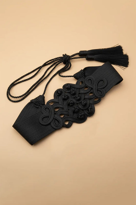 Front view of wide black cord waist belt with adjustable tassel ties on beige background.
