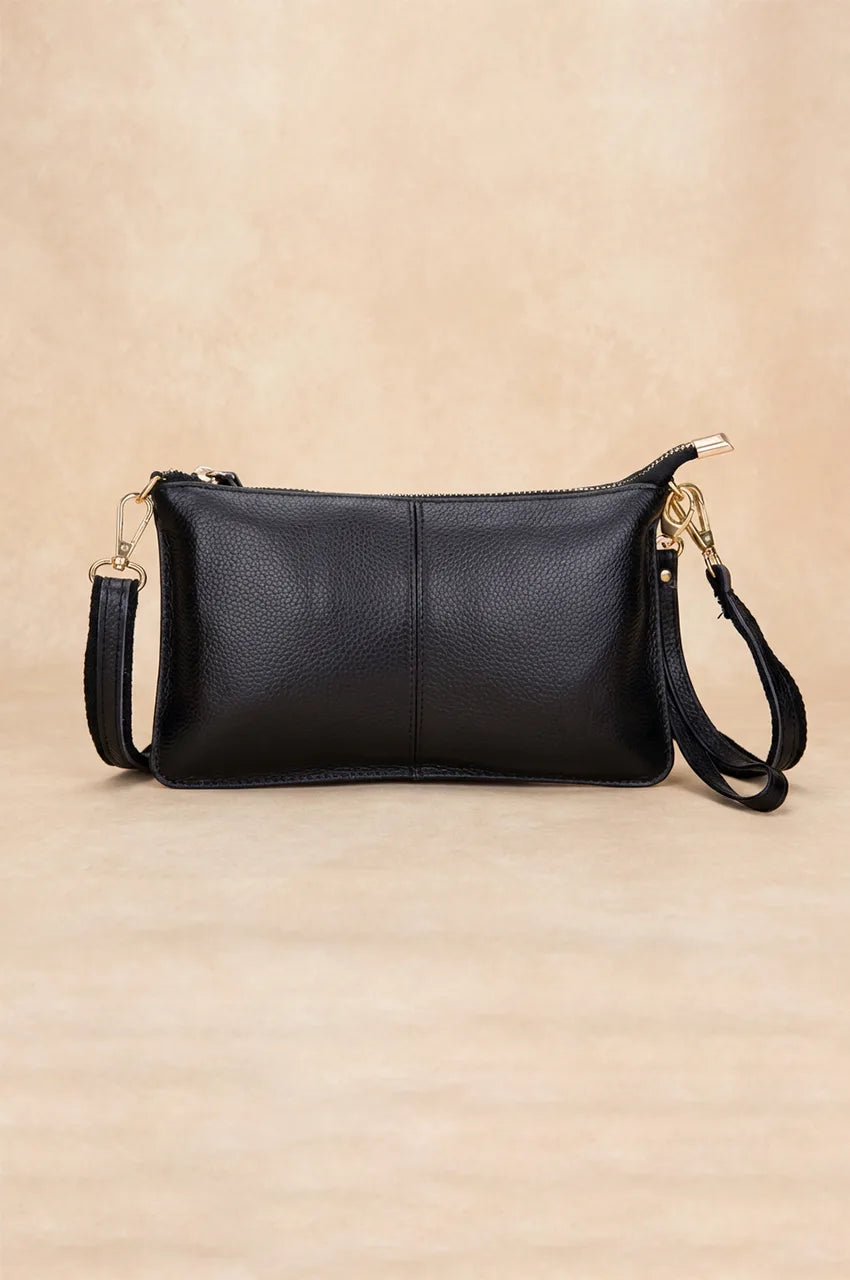 Front view of the black genuine leather crossbody clutch with gold hardware on a beige background.