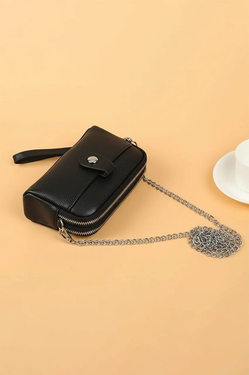 Angled side view of black leather wristlet wallet showing pebbled texture and detachable silver chain strap.