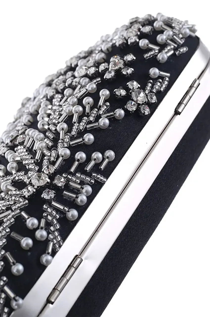 Angled top view of black oval minaudière highlighting the dense floral pattern of crystals and pearls against dark fabric.