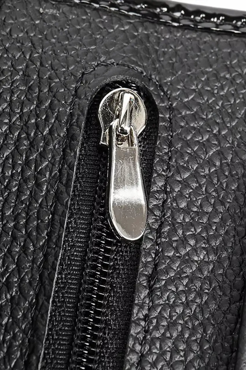 Macro detail of the sleek silver-tone zipper pull on the black textured patent leather wallet clutch.
