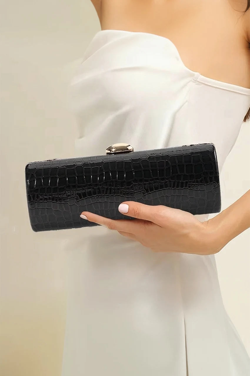 Woman holding a black patent leather cylinder evening bag styled with a white cocktail dress.
