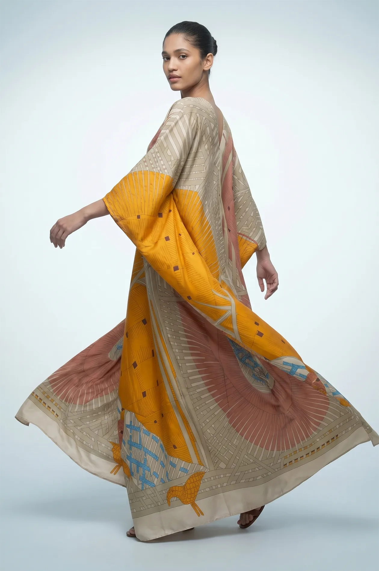 Woman twirling in green silk kaftan with kimono sleeves and bird print