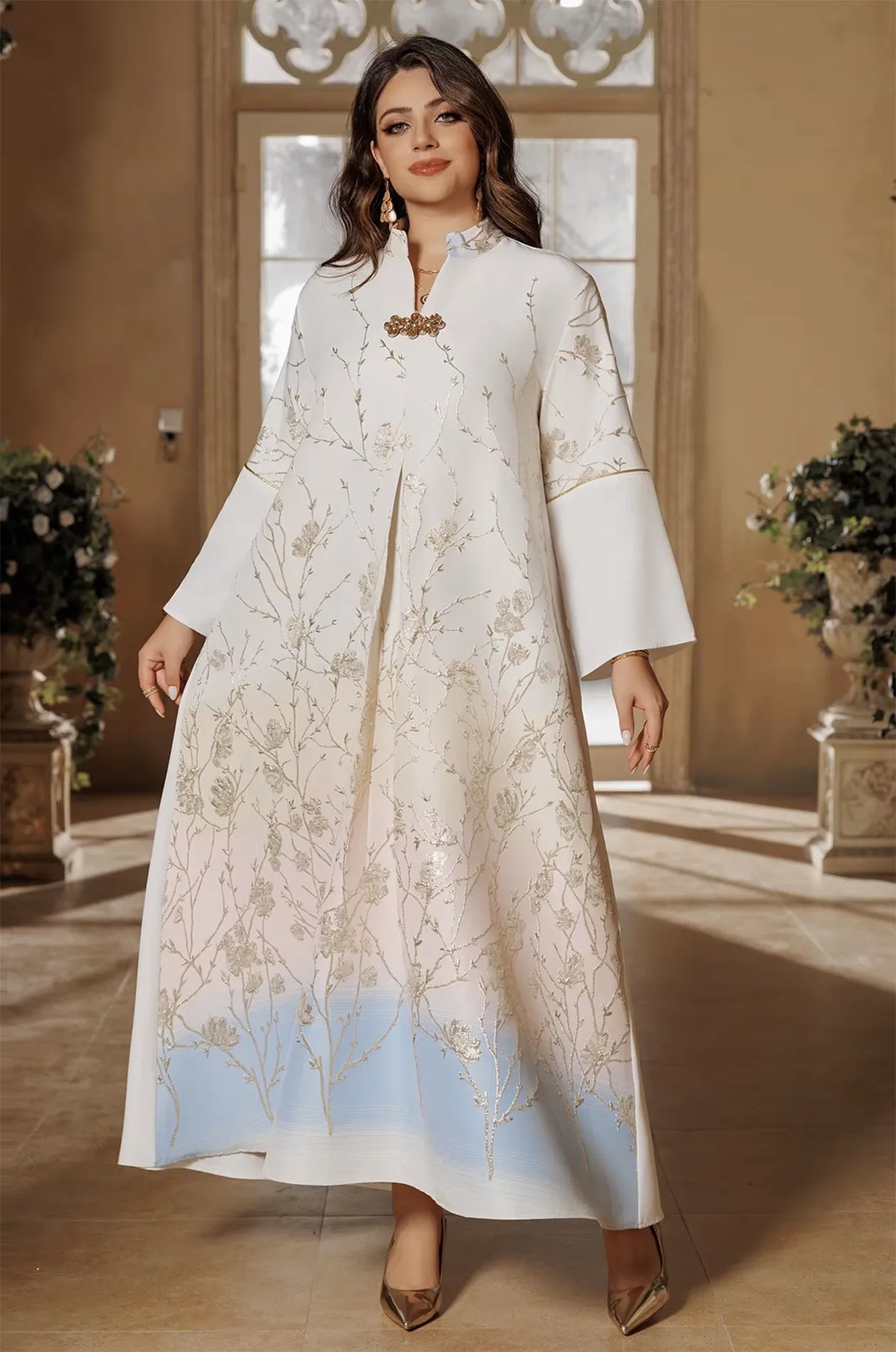 The Tayla Botanical Kaftan in Light Blue displayed in a luxury setting, highlighting the shimmering silver vines and sky-blue ombré hem.