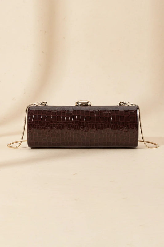 Front view of the Naylara burgundy patent leather cylinder clutch with gold clasp on a beige background.