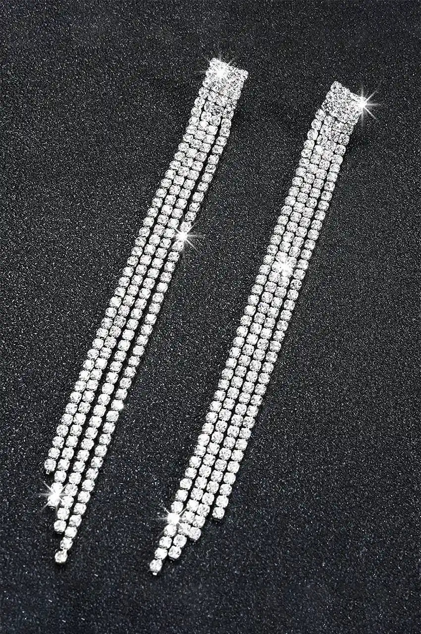 High contrast flat lay of sparking crystal fringe earrings on a dark textured surface.