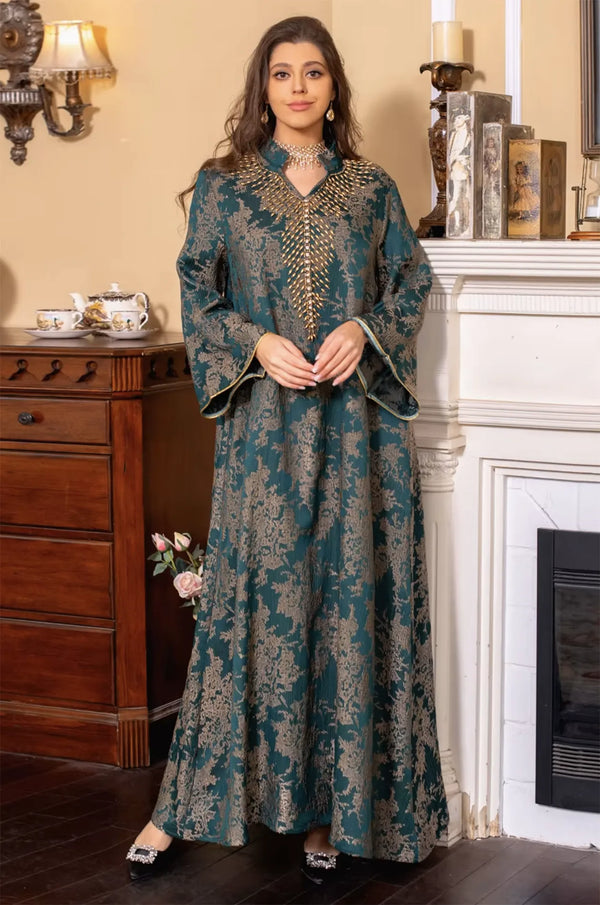 Lifestyle shot of the Estel dark green kaftan with the model standing in a luxury interior near a classic fireplace mantel.