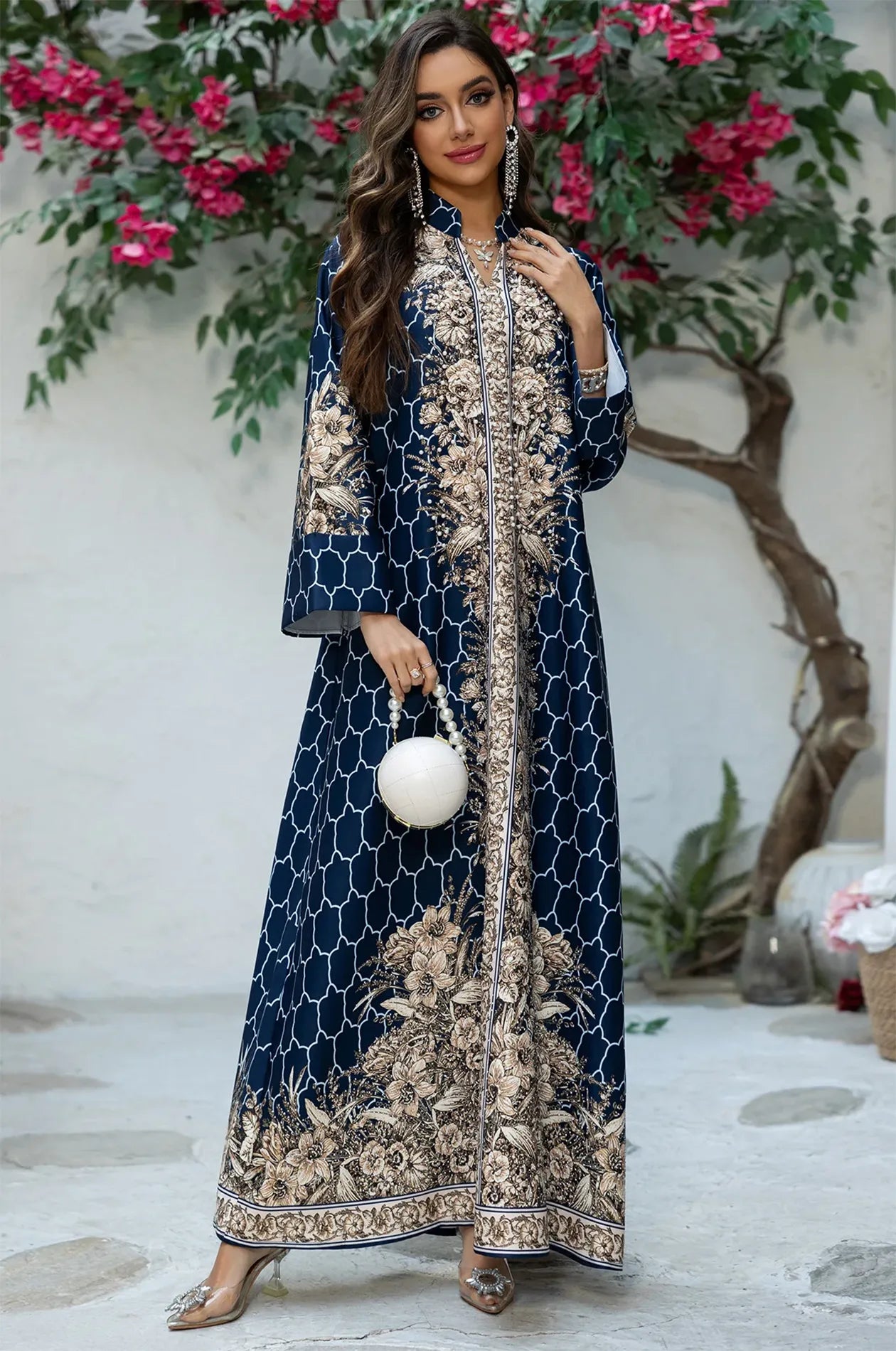 Model wearing the Elora Blue traditional Turkish kaftan in a garden setting, styled with a white spherical pearl clutch.
