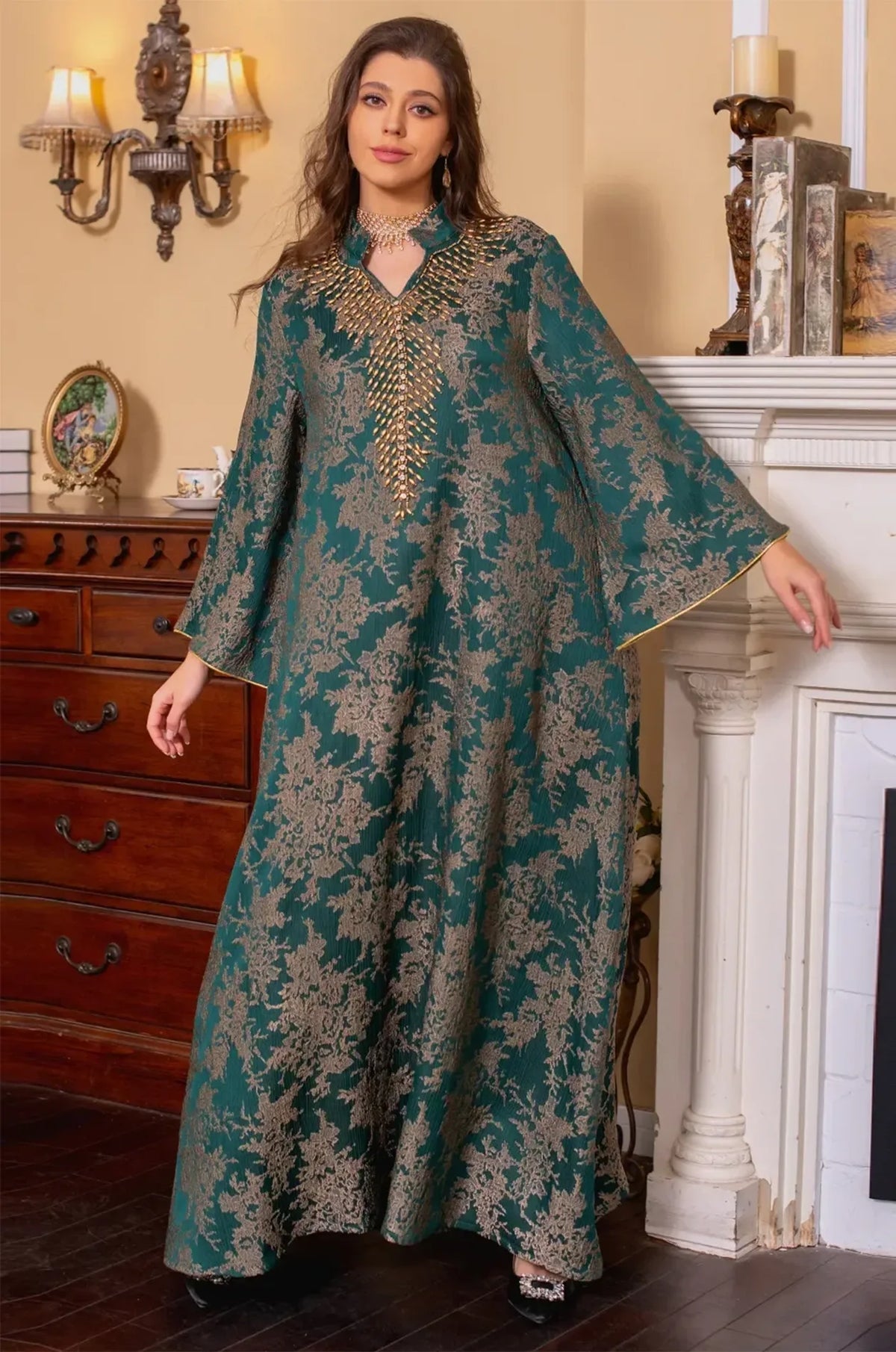 Full-length view of the model in the dark green Estel kaftan, posed gracefully near a white fireplace in a refined interior.
