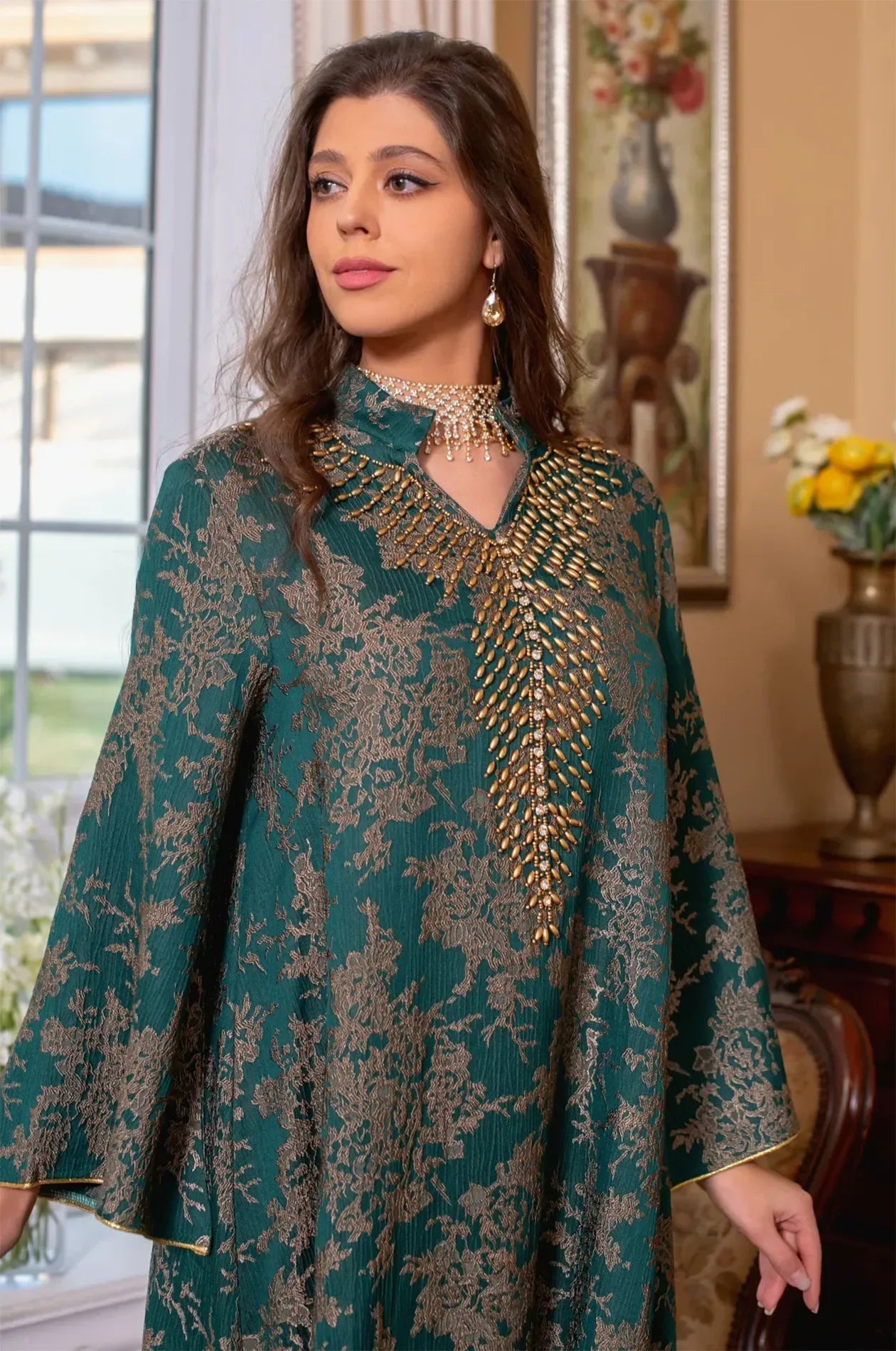 Close-up portrait focusing on the intricate gold beadwork and high V-neck collar of the dark green Estel kaftan.
