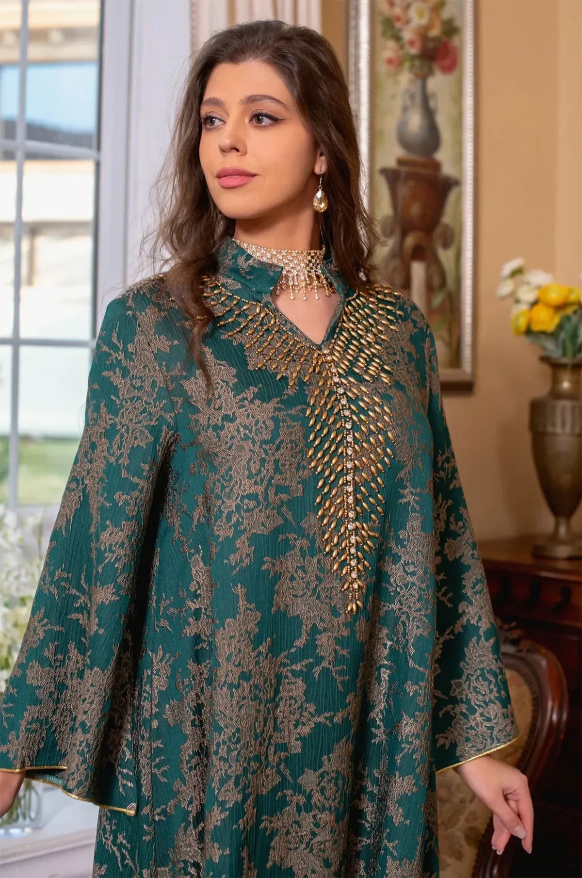 Close-up portrait focusing on the intricate gold beadwork and high V-neck collar of the dark green Estel kaftan.