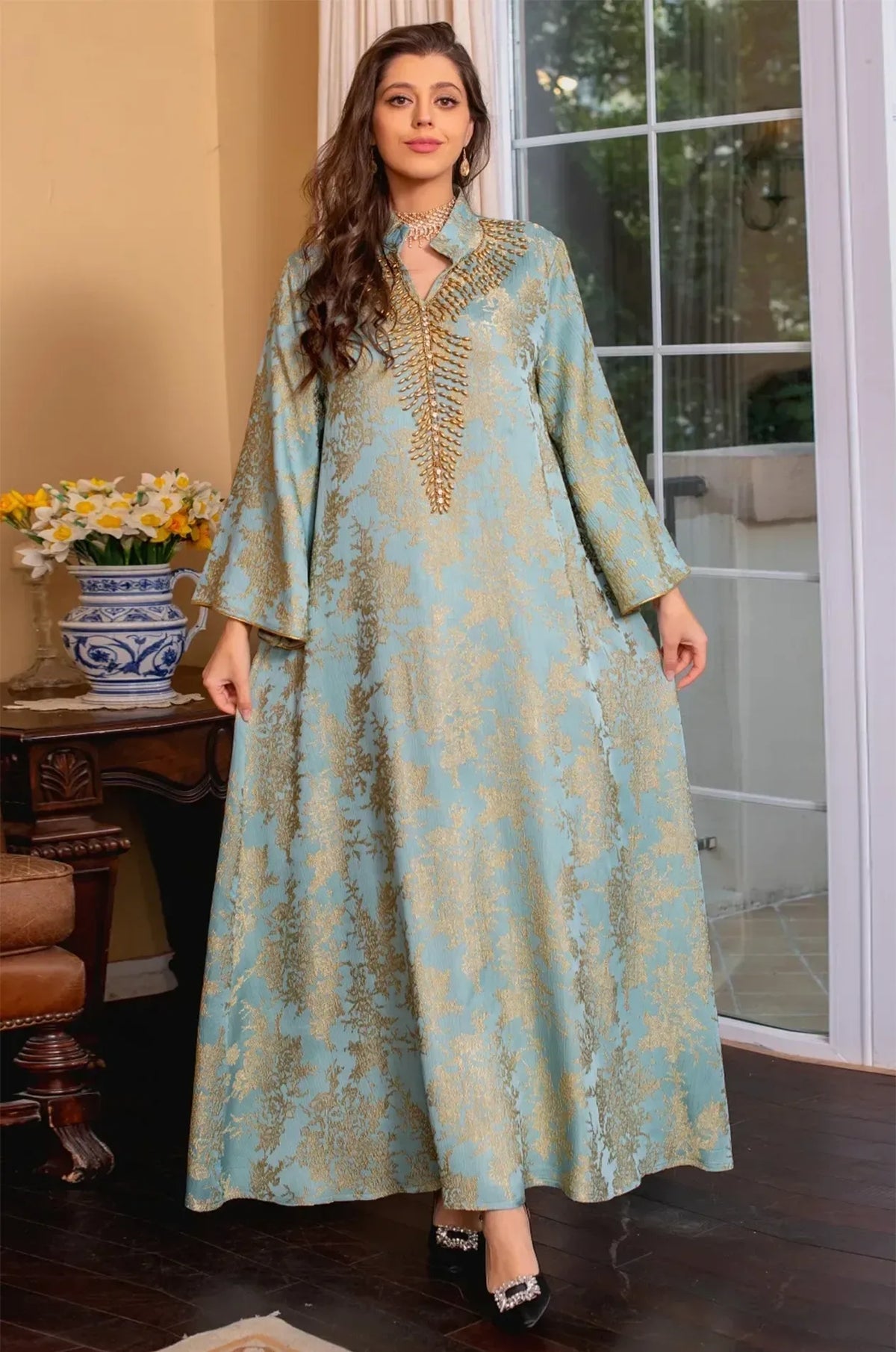 Full-length shot of the model holding the sides of the light blue Estel kaftan to show the flowing jacquard fabric.
