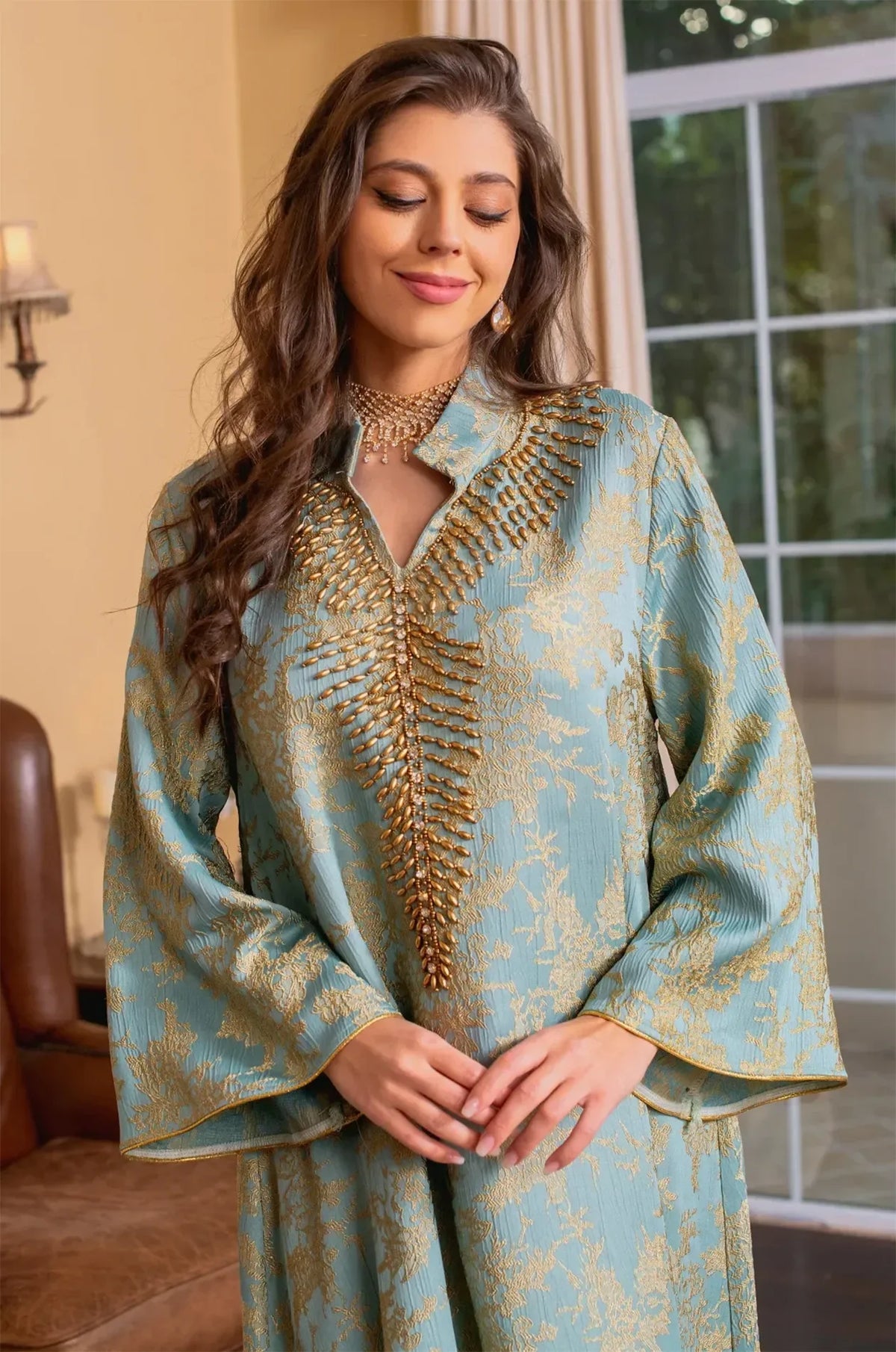Medium shot of the light blue Estel kaftan with the model looking down and hands clasped, highlighting the sleeve details.