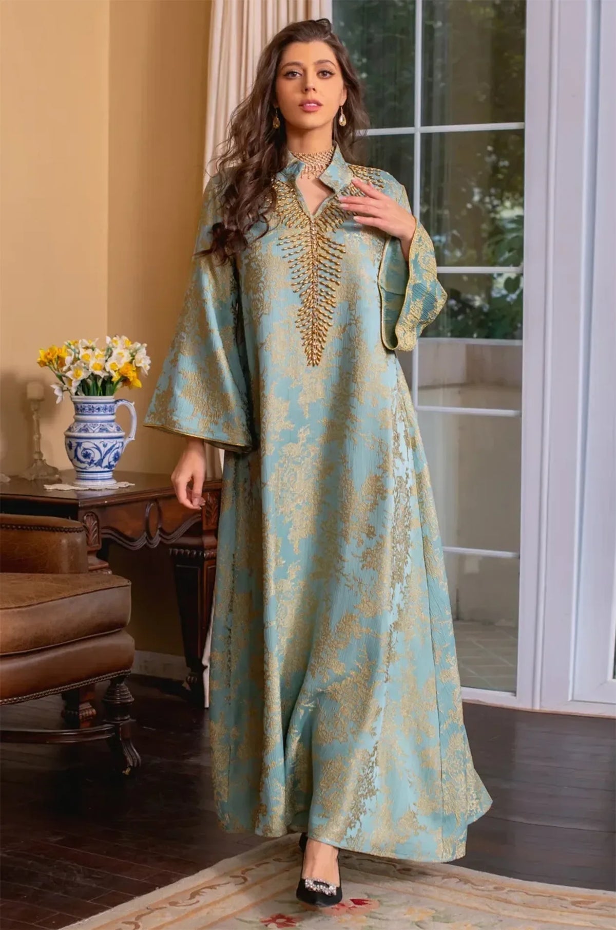 Dynamic walking pose of the model wearing the light blue Estel kaftan in a classic interior near a vintage fireplace.