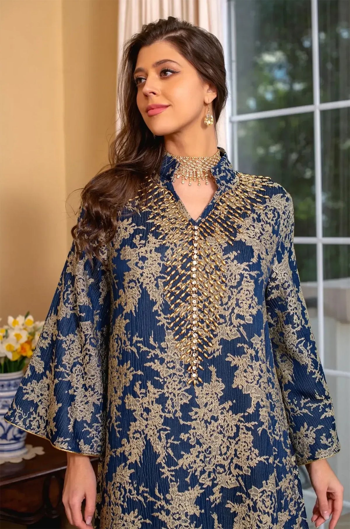 Close-up portrait shot focusing on the intricate gold cascading beadwork and V-neckline of the navy blue Estel kaftan.