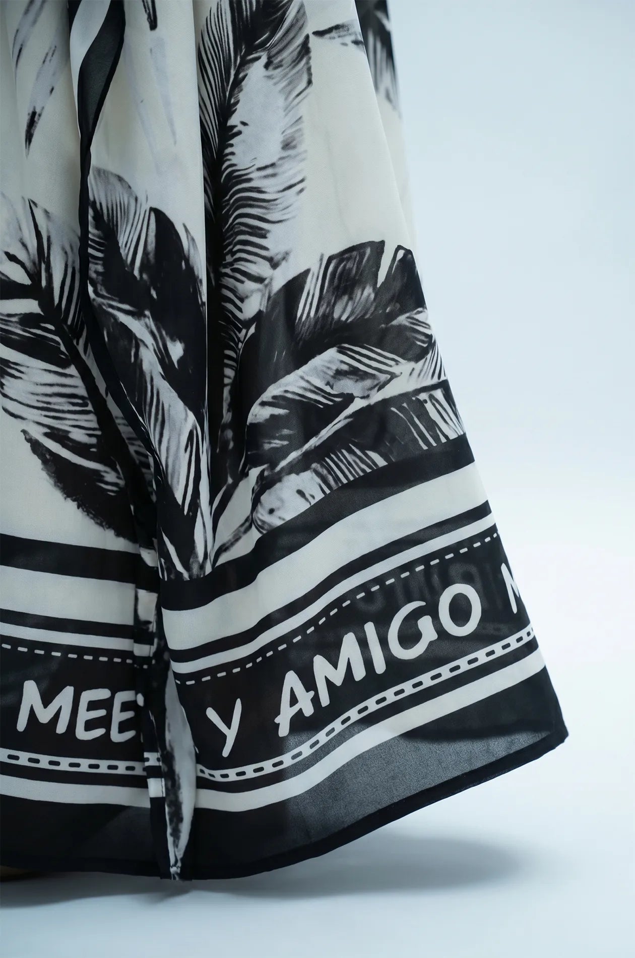 Hem detail of flamingo kaftan with black palm print and scarf-style border