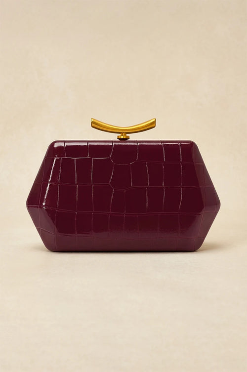 Front view of isolated burgundy geometric box clutch with crocodile texture and curved gold metal handle.