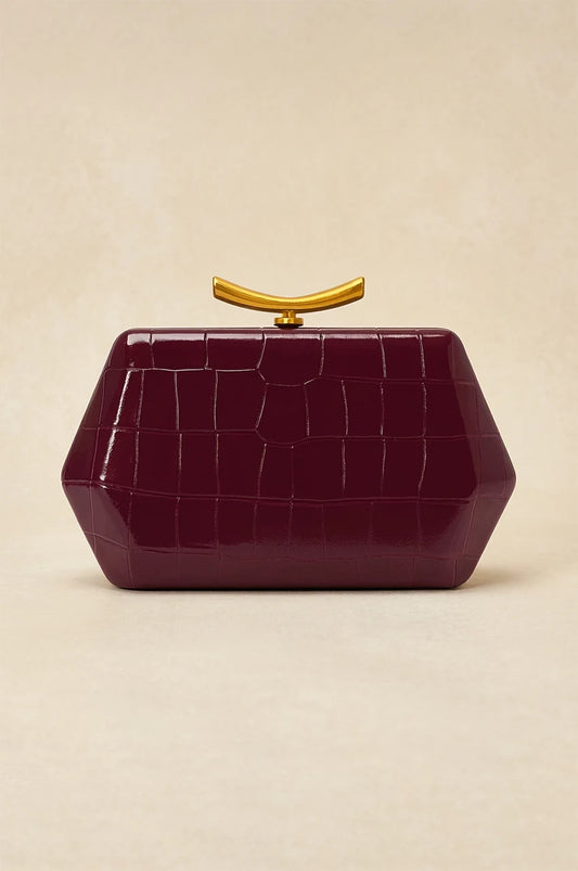 Front view of isolated burgundy geometric box clutch with crocodile texture and curved gold metal handle.