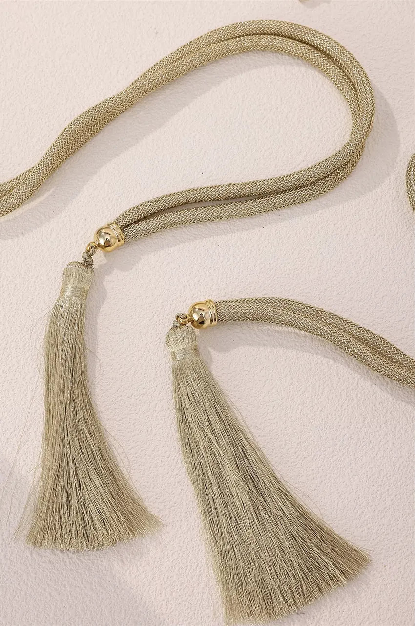 Close-up of gold braided rope ties and metallic-capped tassels on the geometric chain belt.